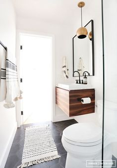 a white toilet sitting next to a bathroom sink under a mirror on top of a wooden cabinet