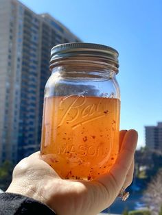 a person holding up a jar filled with liquid in front of a cityscape