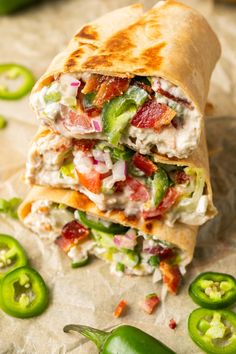 a chicken salad wrap cut in half and stacked on top of each other next to green peppers