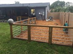 a fenced in area with wood chips on the ground and a dog house behind it