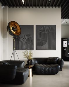 a living room with black leather couches and art on the wall