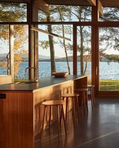 a kitchen with lots of windows and wooden furniture next to the water's edge