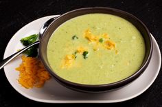 a bowl of broccoli soup next to some carrots on a white plate