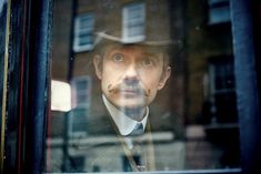 a man with a mustache and hat looking out the window at something in front of him