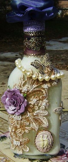 a decorative bottle with purple flowers and pearls on it's side sitting on a table