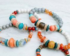 "Set of five stack bracelets for resale. Bulk discount for this listing, additional discounts will not apply. Listing as shown.  Brilliant orange, sandy beige, beautiful rich reds, caramel, turquoise and green. Contrast, texture, and interest. 7.0\" to 7.5\" in length. Beautiful handmade lampwork beads, recycled African glass, metal accents, Turquoise, Carnelian, Red Jasper, African fused glass, coconut heishi, dyed wood and more. Each one-of-a-kind. The bracelets pictured is the listing are the Stackable Orange Round Beaded Bracelets, Orange Stackable Bracelets With Round Beads, Orange Stackable Beaded Bracelets As Gift, Orange Stackable Beaded Bracelets For Gifts, Contrast Texture, Margarita On The Rocks, Stack Bracelets, Rock Necklace, Handmade Lampwork Bead