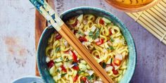 two chopsticks in a bowl of noodles with vegetables and sauce on the side