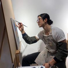 a woman is painting on an easel while holding a paintbrush in her hand