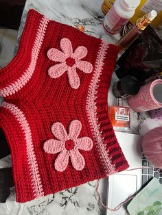 a crocheted red sweater with pink flowers on it and some yarn next to it