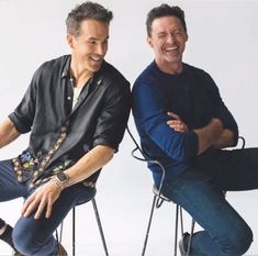 two men sitting on chairs with their arms crossed and one man is smiling at the camera