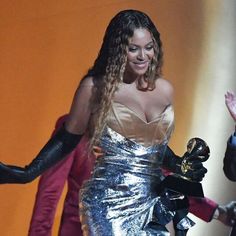 a woman in a silver dress and black gloves is holding her hand out to someone