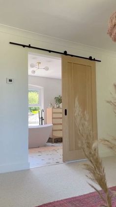 an open door leading to a bathroom with a bathtub in the background and a pink rug on the floor