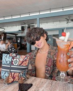 a man sitting at a table with a drink in his hand and a bag on the other side