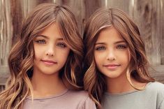 two beautiful young women standing next to each other in front of a wooden fence and looking at the camera