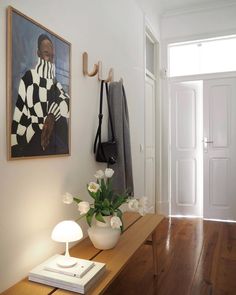 a painting hangs on the wall next to a table with flowers and a coat rack