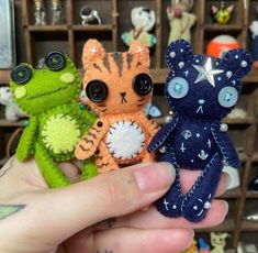 three small stuffed animals are being held in front of a shelf filled with other items