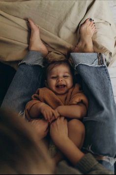 a baby crying while laying on top of someone's lap in bed with their feet up