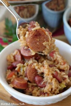 a spoon full of rice and sausage with other food items in the bowl behind it