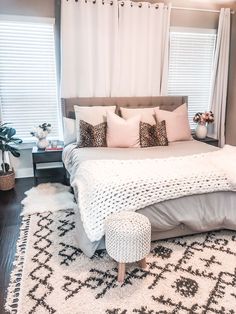 a bedroom with a large bed and white rugs on the floor in front of two windows