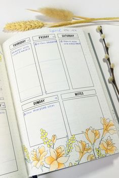 an open planner with yellow flowers on it and a plant next to it in front of the page