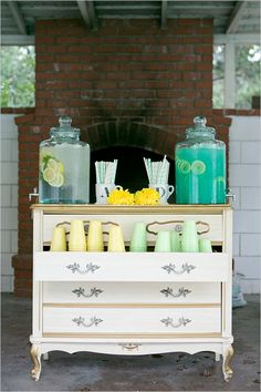 a white dresser with yellow and green candles on the top, next to some bottles