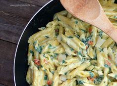 a pan filled with pasta and spinach on top of a wooden table