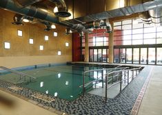 an indoor swimming pool with tiled flooring and metal railings, surrounded by large windows