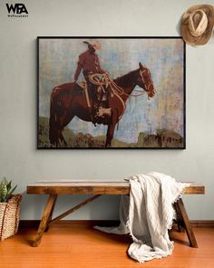 a painting hanging on the wall above a wooden bench with a cowboy hat and boots