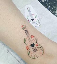 a woman's foot with a guitar tattoo on her left leg and flowers around it