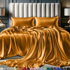 a bed covered in gold sheets and pillows next to a night stand with two lamps