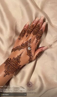 a woman's hand with henna tattoos on it and her hands resting on the bed