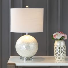 a table with a lamp, vase and flowers on it next to a gray wall