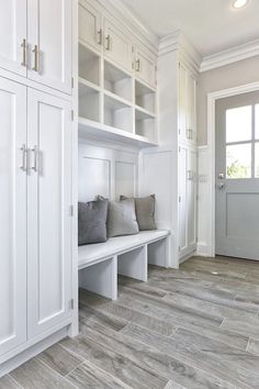 a room with some white cabinets and gray pillows on the bench in front of it