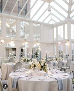 a table set up with white flowers and candles for a wedding reception in a glass walled room