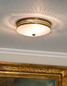 a ceiling light that is on in a room with a painting and framed pictures behind it