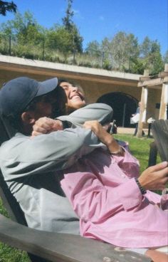 two people sitting on a bench in the grass and one person taking a selfie