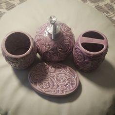 three pink vases sitting on top of a white bed next to a cup and saucer