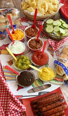 hot dogs, chips and condiments on a table with red checkered cloth