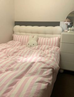 a bed with a pink and white striped comforter on top of it next to a night stand