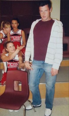 a man standing in front of a group of young people wearing cheerleader shirts and jeans