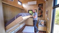 a man standing next to a bunk bed in a room with wooden walls and flooring