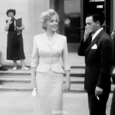 black and white photograph of woman in formal dress talking on cell phone with man standing next to her