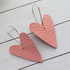 two heart shaped pink leather earrings sitting on top of a white wooden table next to a plant