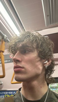 a young man with curly hair on a subway train looking off to the side while listening to earbuds