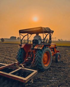 an orange tractor pulling a plow in the middle of a farm field at sunset