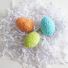 three crocheted eggs sitting on top of white shredded paper next to each other