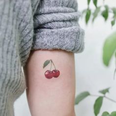 a small cherry tattoo on the left inner arm, with two cherries attached to it