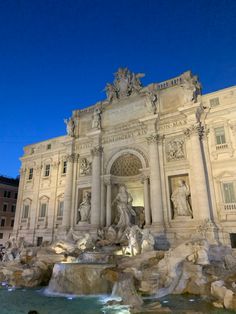 people are standing around in front of a building with statues on the sides and fountains