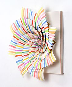 an art piece made out of colored paper on a white wall with a book in the background