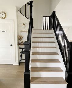 there is a clock on the wall next to some stairs in this house with white walls and black railings